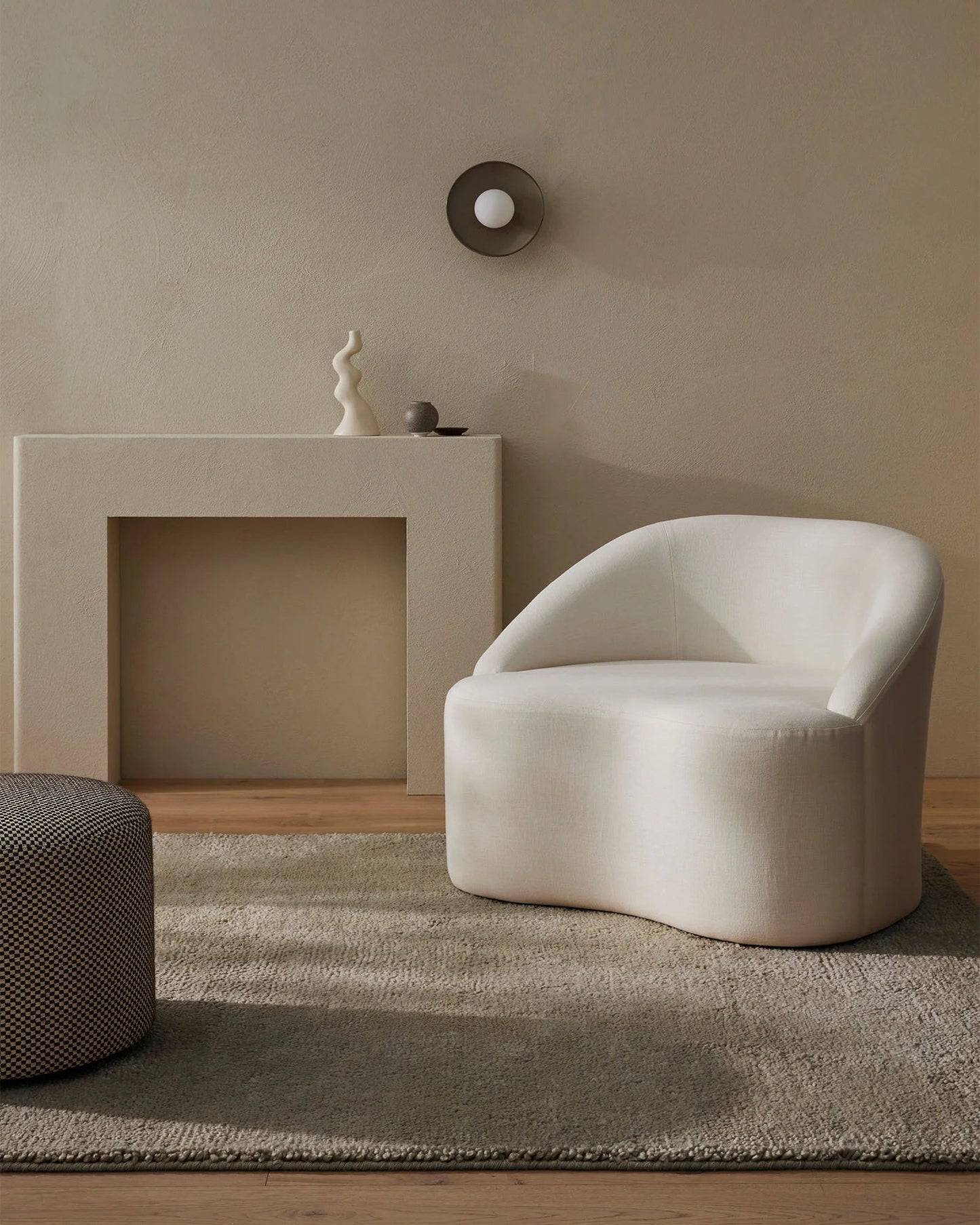 A well-appointed room featuring a modern white chair and a minimalist design. The room includes a modern fireplace, a decorative object on the mantel, and a large area rug in a neutral shade, providing a serene and elegant atmosphere.